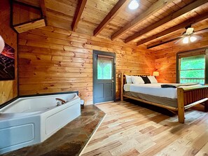 A cabin with a wooden interior, a bed, a bathtub, and a ceiling fan.