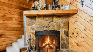 Una chimenea de piedra con fuego, escalones de madera que llevan a ella y un techo de madera.
