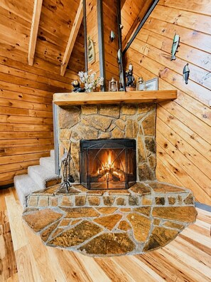 Ein Kamin aus Stein mit Feuer, Holzwandstufen führen hinauf und eine Holzbalkendecke.