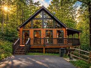 A log cabin with a balcony, a stone foundation, and a wooden fence.