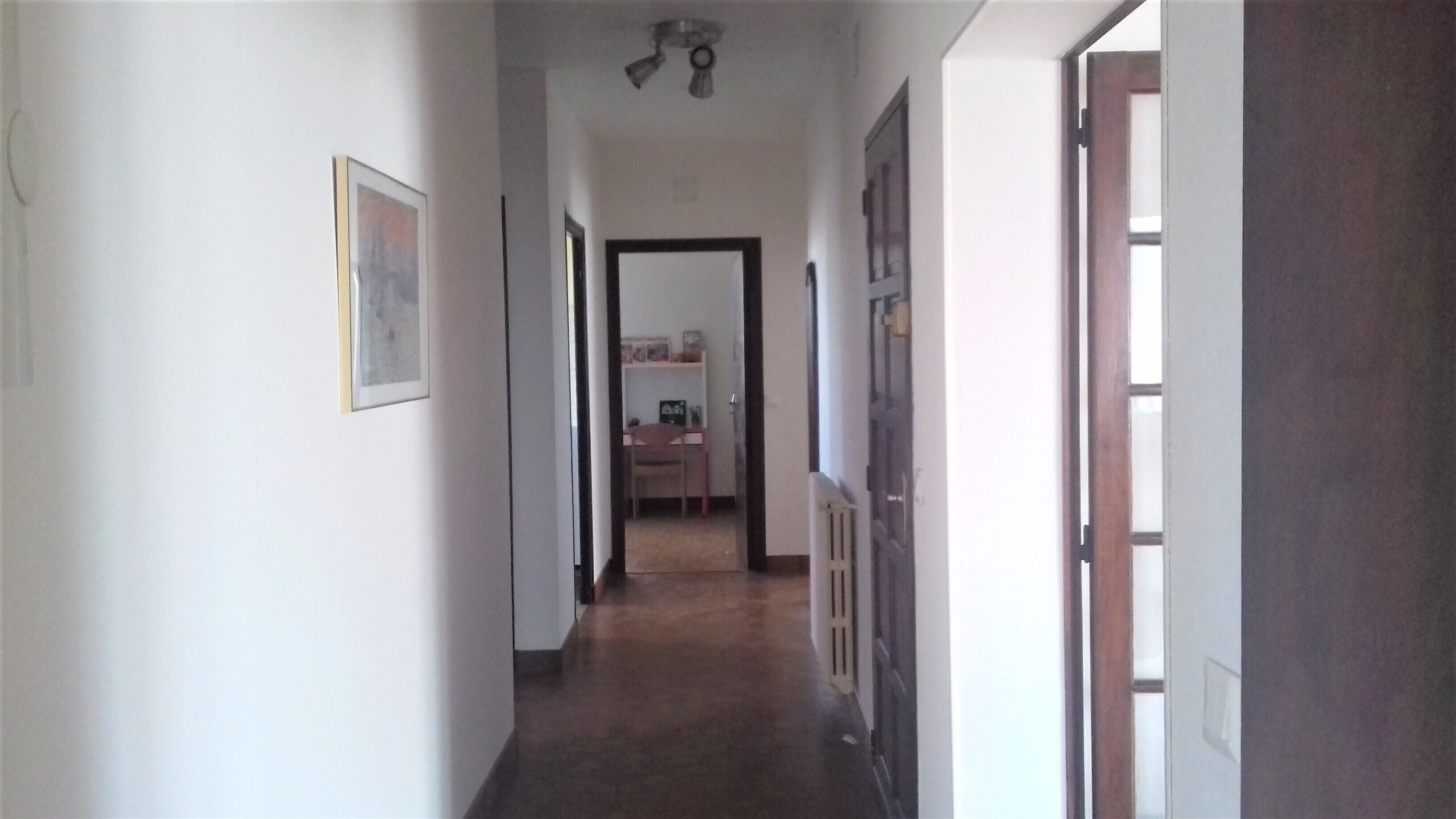 Un couloir étroit avec un ventilateur de plafond, une porte sur la droite et un bureau avec une chaise au fond.