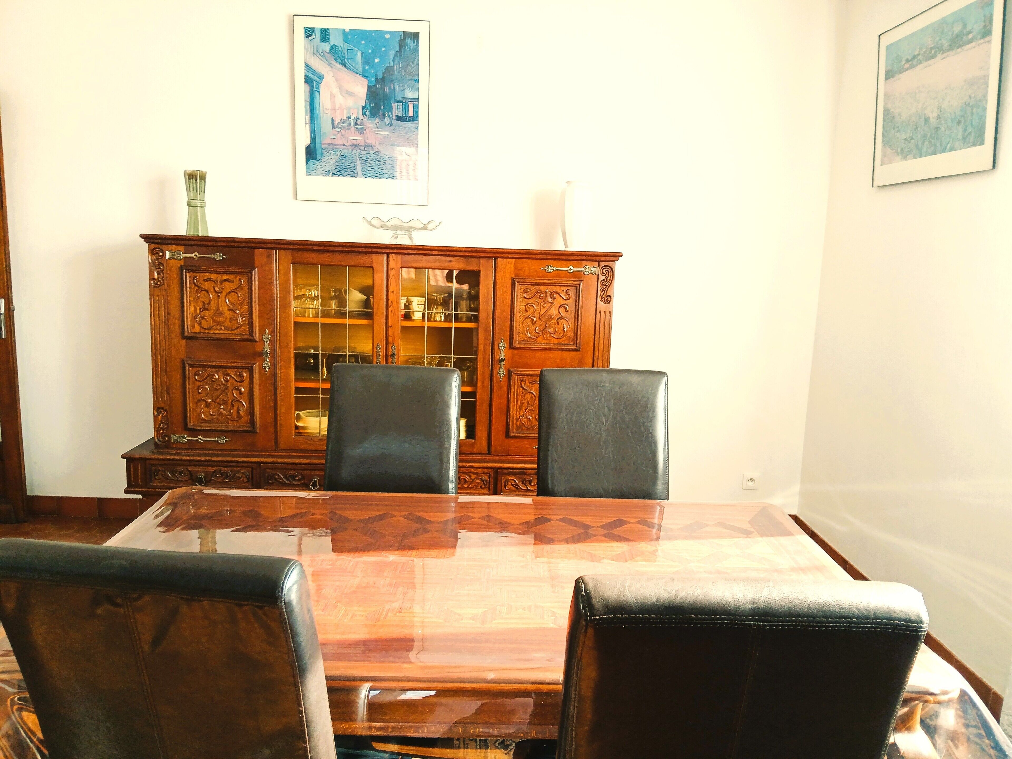 A dining room with a wooden table and chairs, a cabinet with glass doors, and two framed pictures on the wall.