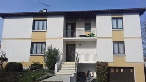 Un edificio de apartamentos de dos pisos con una entrada central, un balcón pequeño en el segundo piso y una reja en la parte delantera.