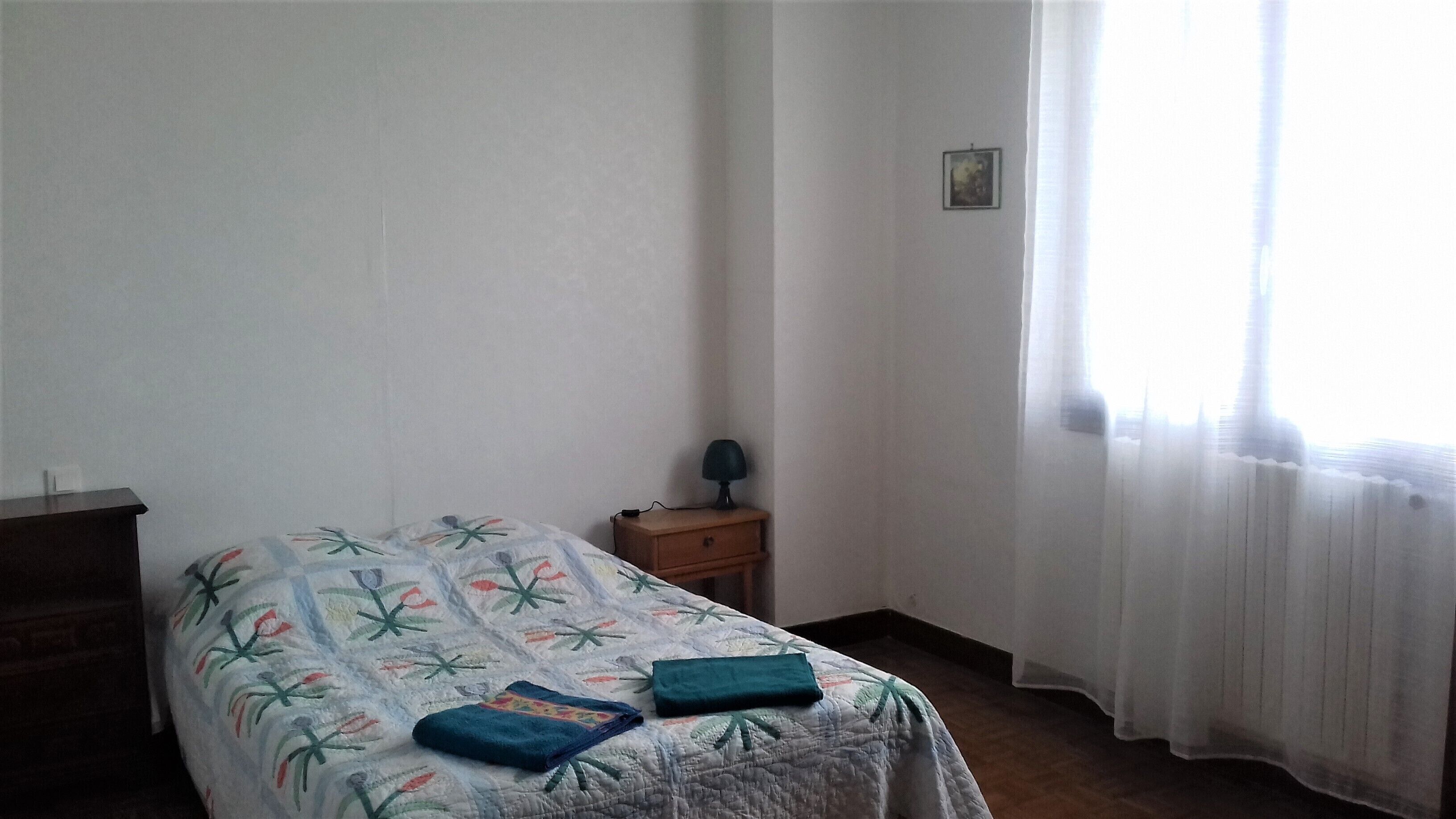 A simple bedroom with a bed, a nightstand, a lamp, and a window with curtains.