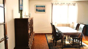 Un comedor con mesa y sillas, un armario, un cuadro en la pared y una ventana con cortinas.