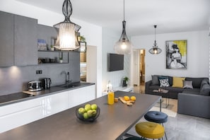 Eine moderne Küche mit einer zentralen Kochinsel, eine Essecke mit einer Couch und ein Wohnzimmer mit Fernseher und Kunstwerken.