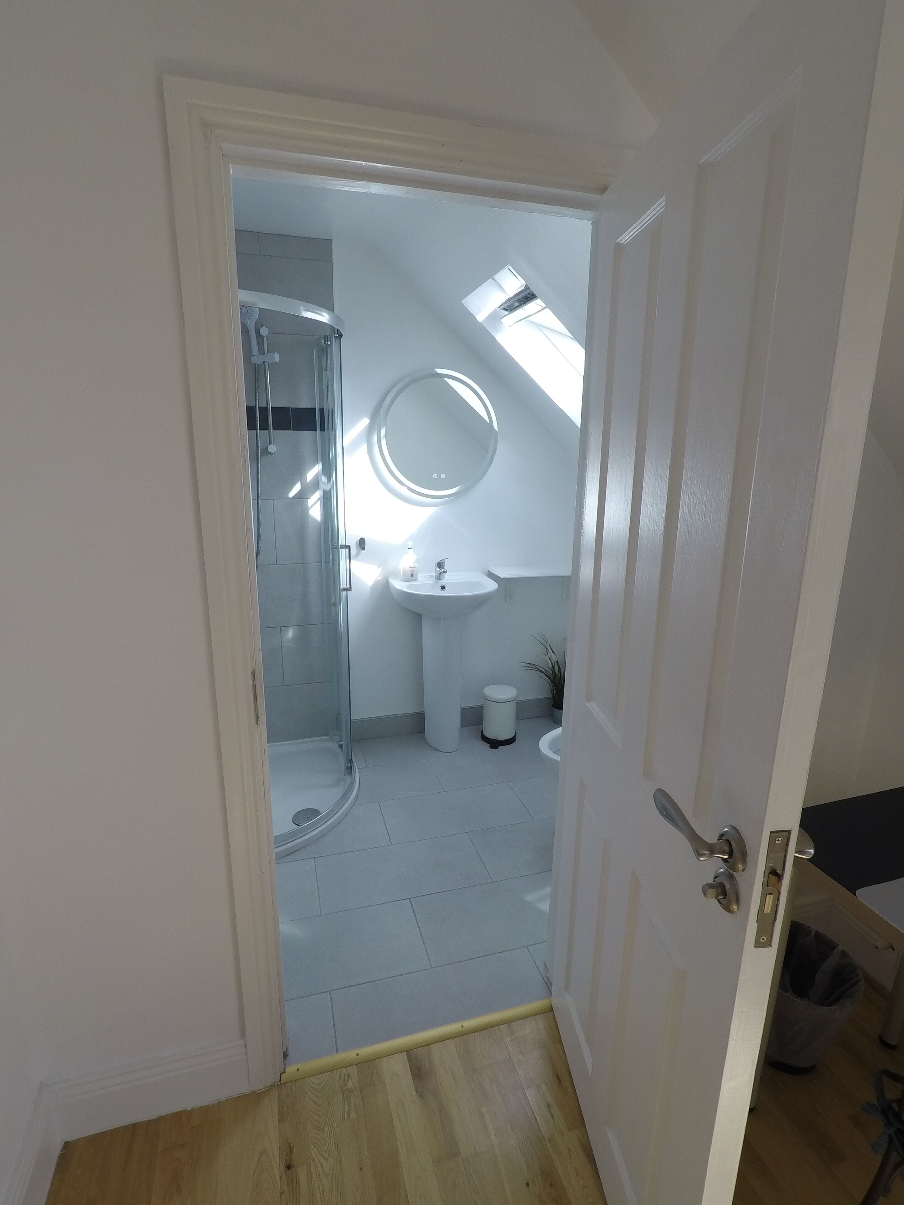 A bathroom with a glass shower, a round mirror, and a sink.