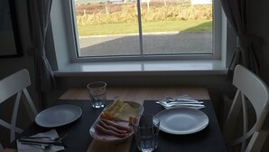 A dining table with plates, cutlery, glasses, and a cheese board set for two. - Seagull Cottage B&B (Portmagee)