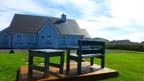 A house with a large lawn, a wooden deck, and a bench. - Seagull Cottage B&B (Portmagee)