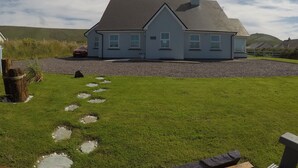 A house with a sloped roof, a gravel driveway, and a grassy lawn with stepping stones. - Seagull Cottage B&B (Portmagee)