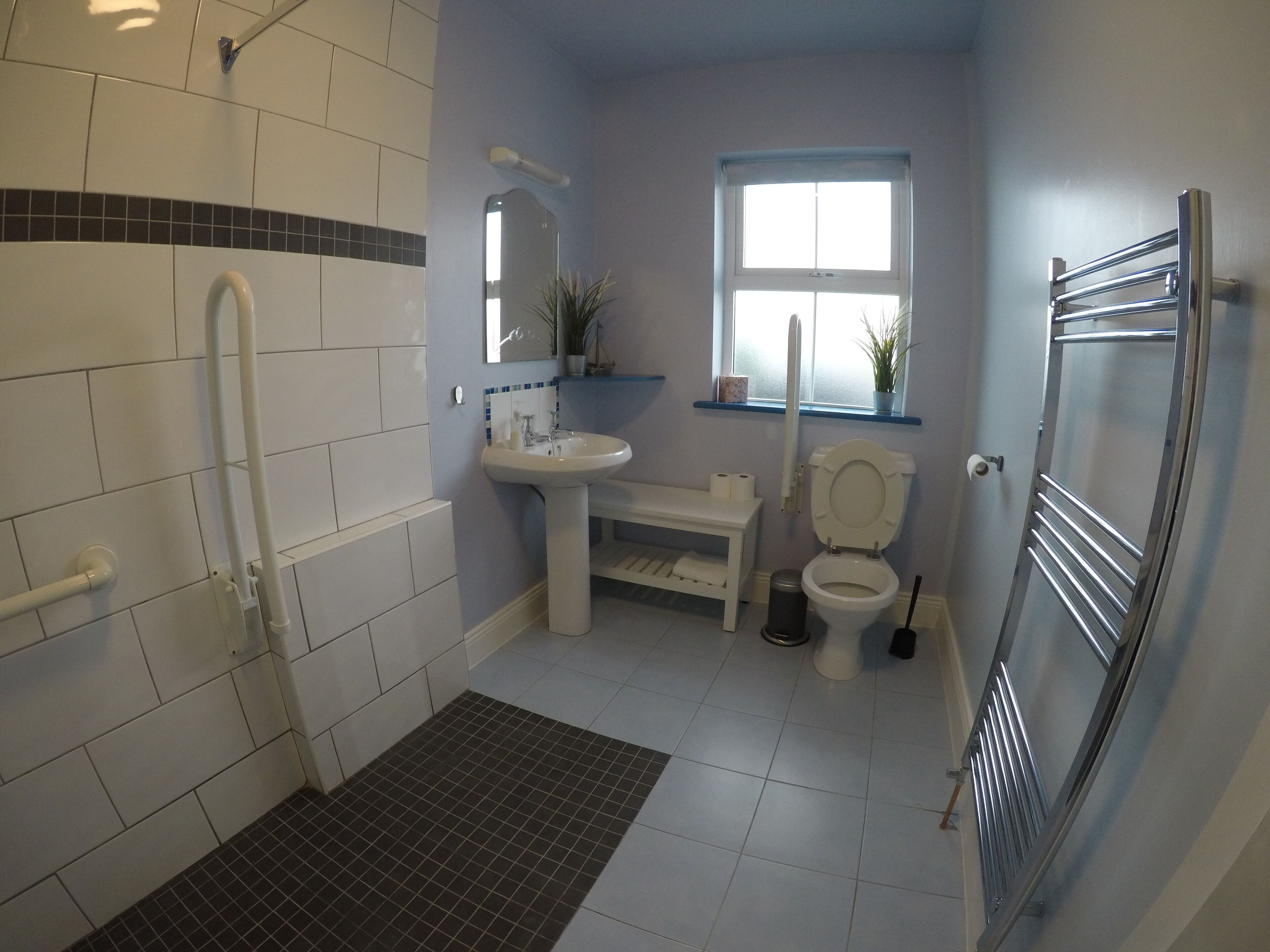 Une salle de bain avec des carreaux blancs, un lavabo, des toilettes, un miroir, une fenêtre et un espace douche.