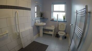 Une salle de bain avec des carreaux blancs, un lavabo, des toilettes, un miroir, une fenêtre et un espace douche.