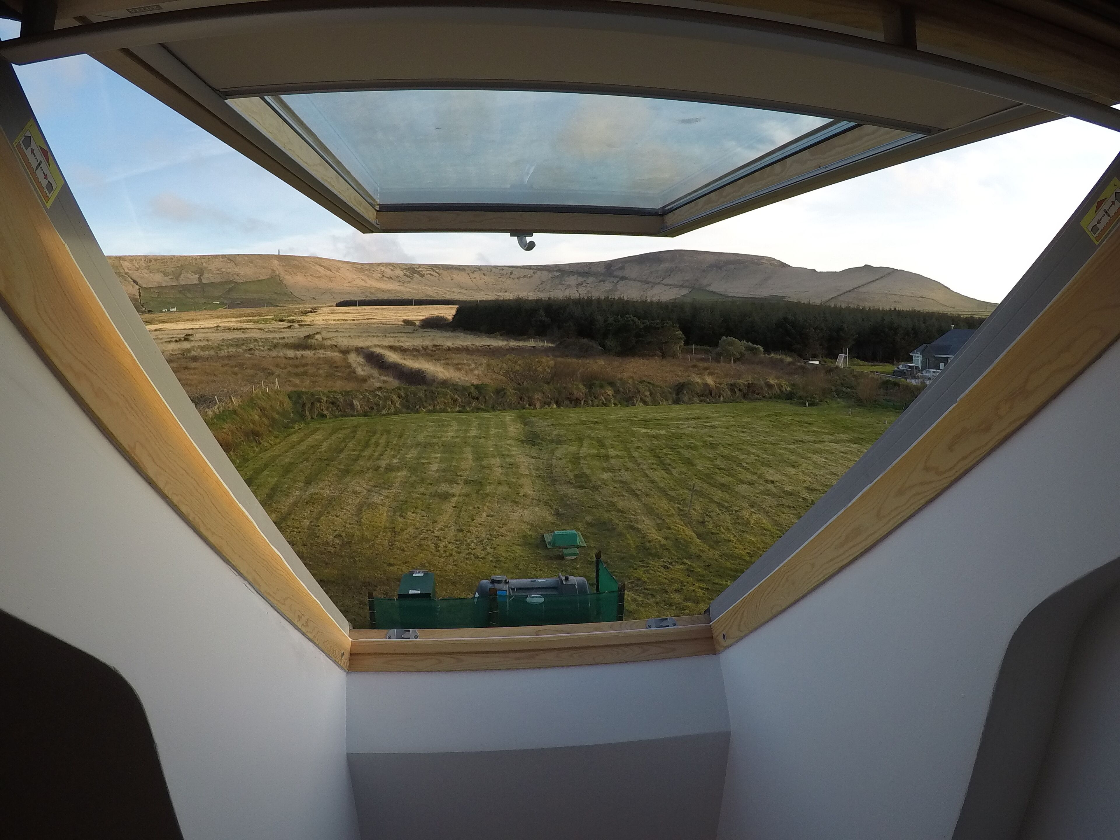 A room with a skylight, a view of a grassy field, and a distant mountain range.