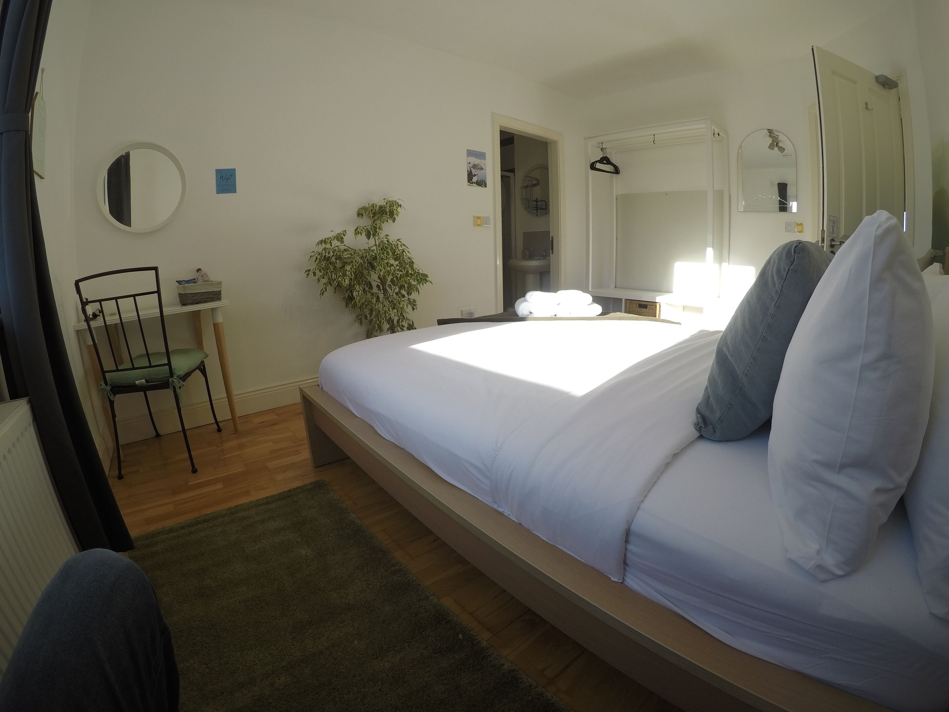 Un dormitorio con una cama, una silla, una mesita, una planta y un espejo.