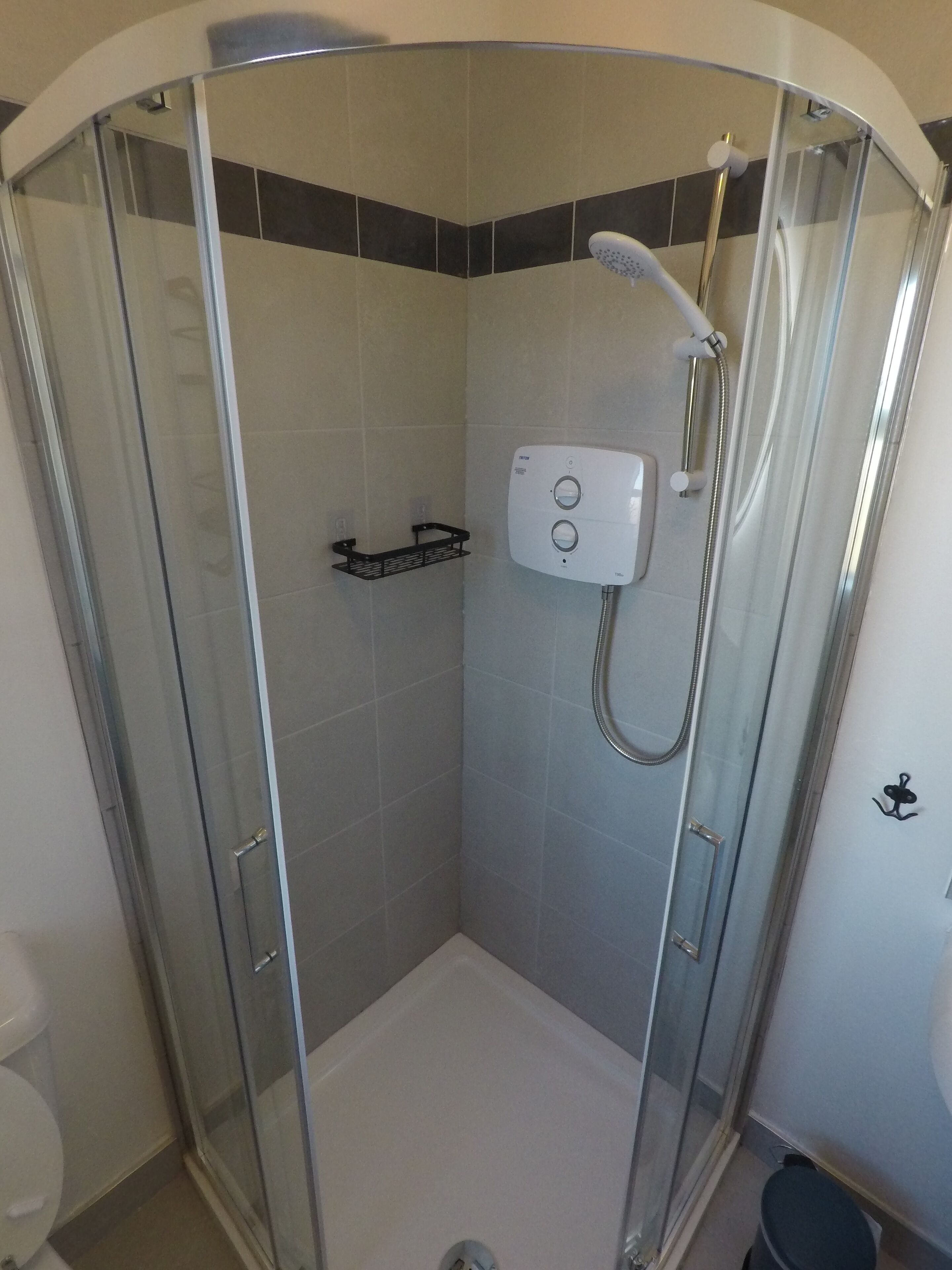 Un vestuario de ducha con paredes de vidrio, un cabezal de ducha manual y un panel de control.