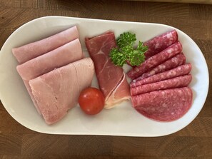 A plate of sliced meats and a tomato on a white plate.