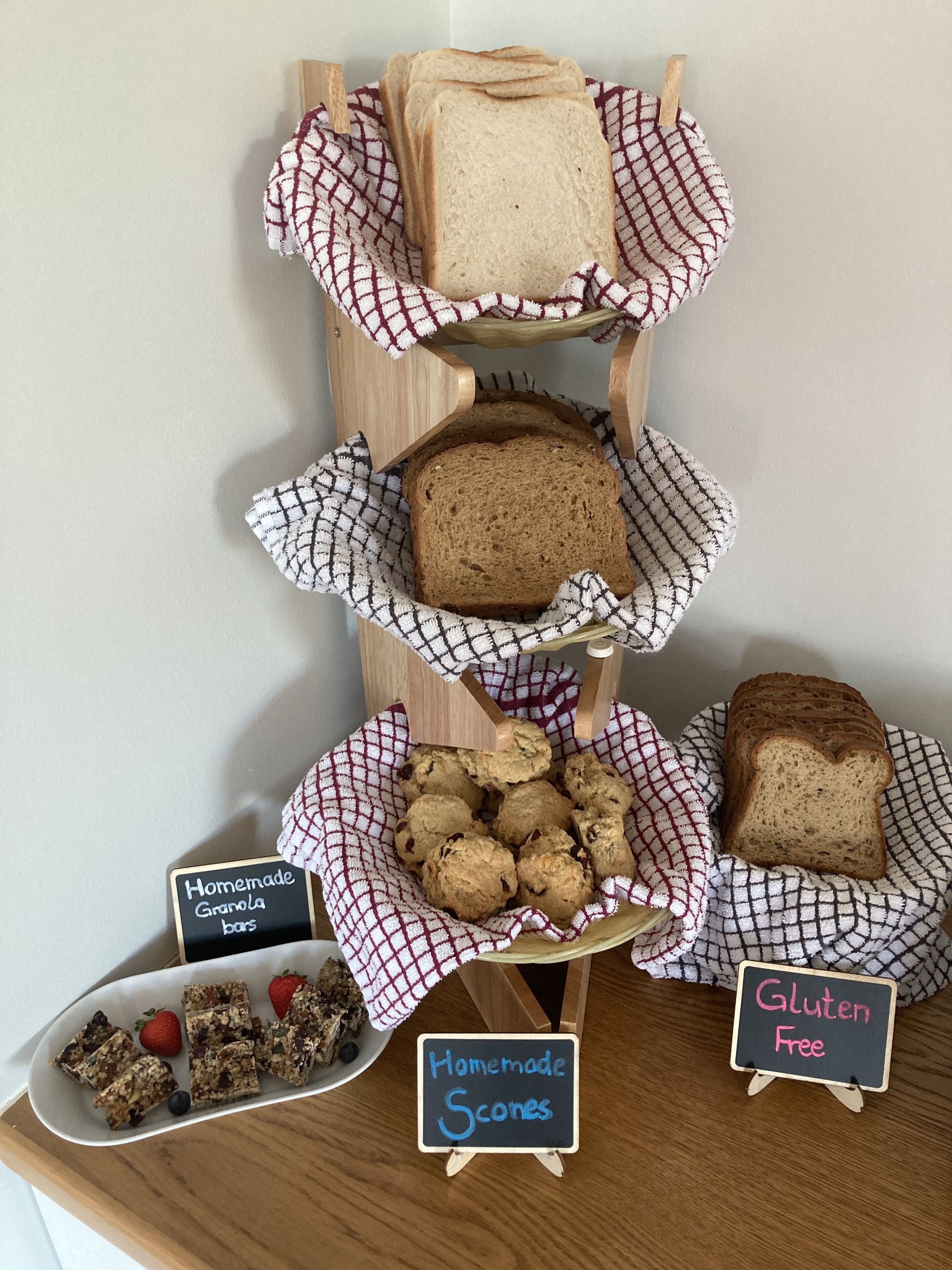 Eine Auswahl hausgemachter Scones, Granola-Riegel und glutenfreies Brot auf einem Holztisch.