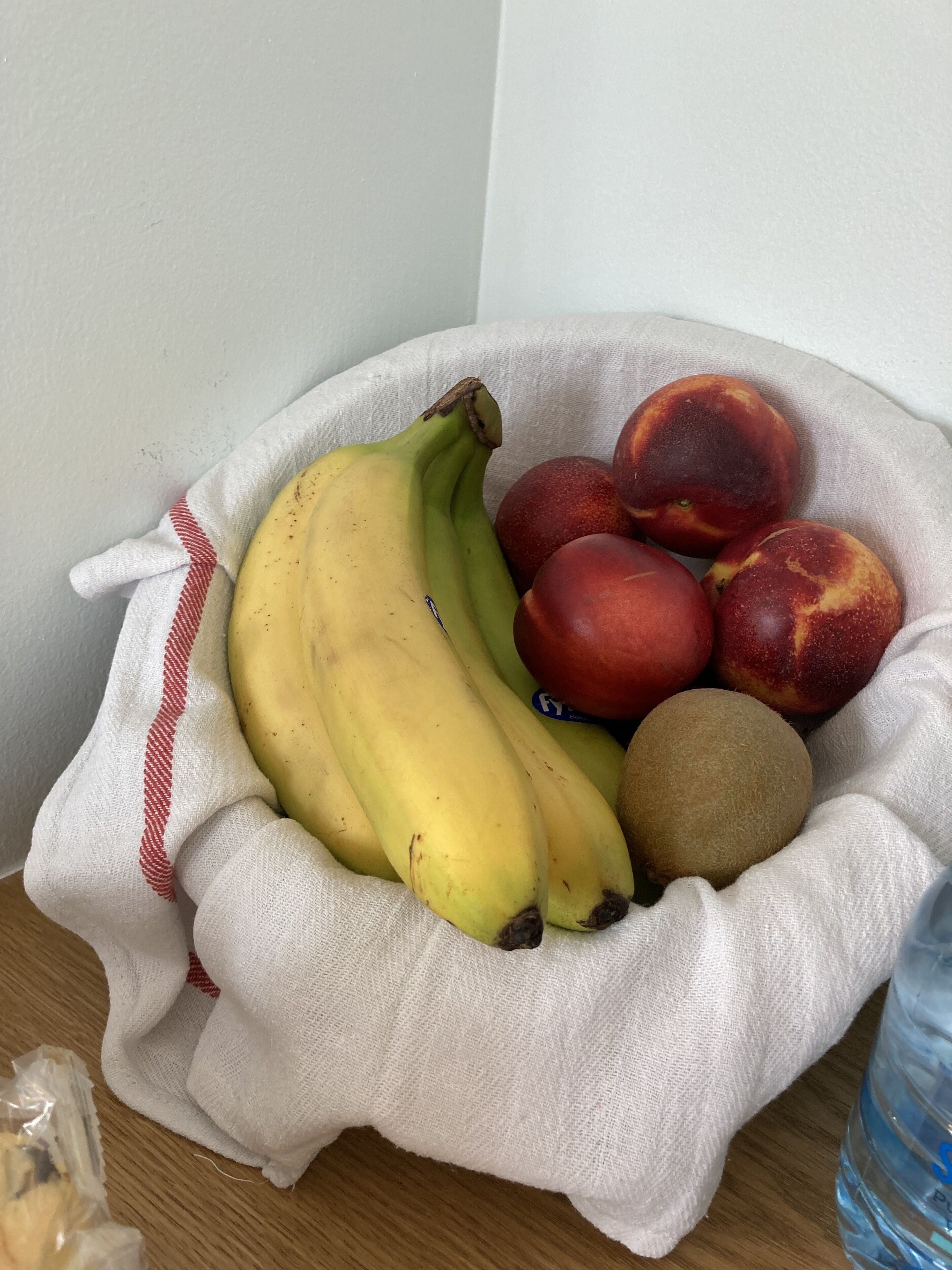 Uma sacola de tecido com bananas, pêssegos e um kiwi sobre uma superfície de madeira.