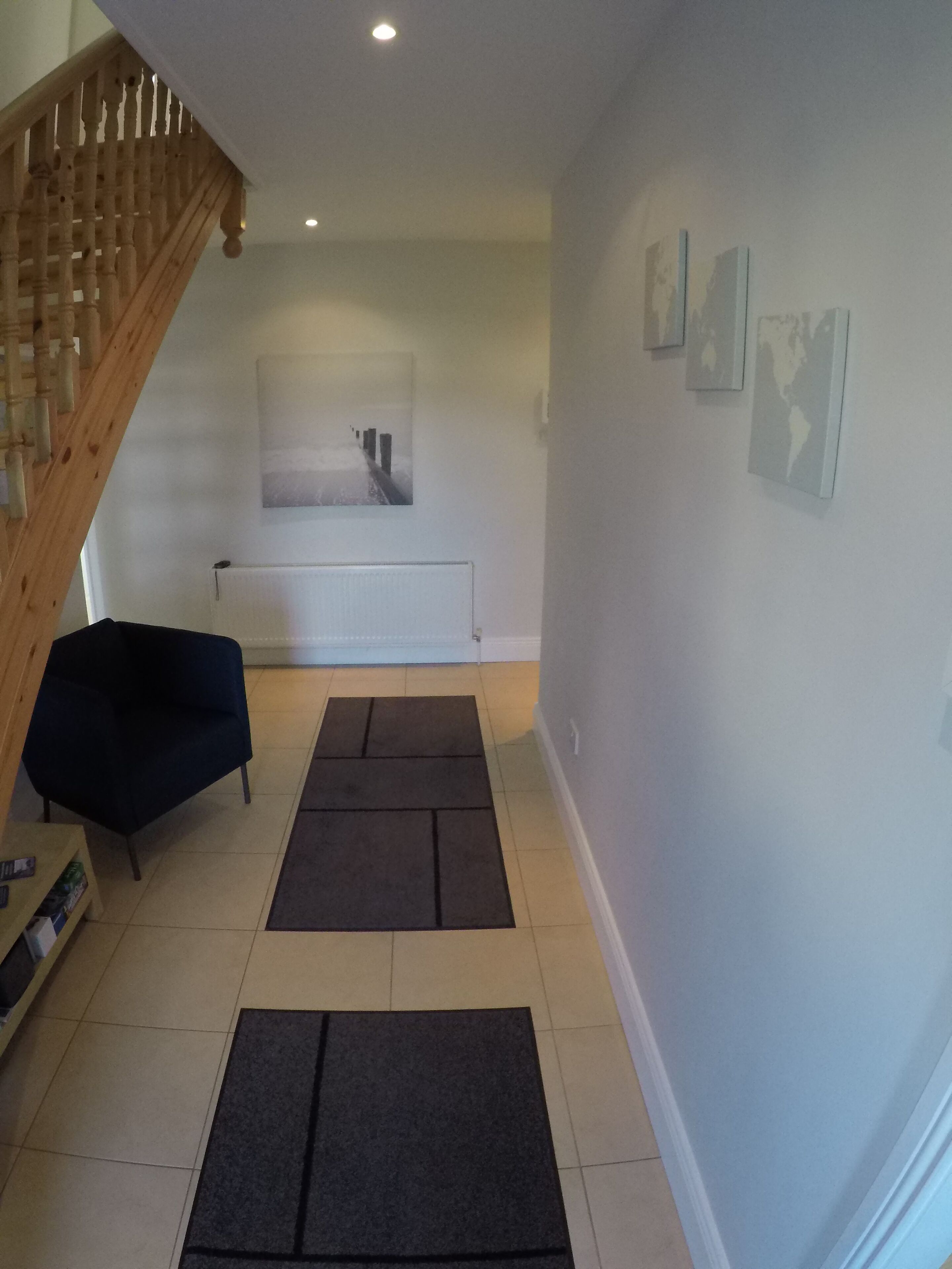 A spacious living area with a wooden staircase, a black sofa, a large painting, and a radiator.