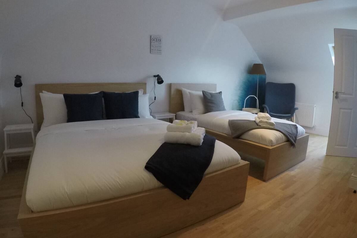 Quarto de hotel moderno com duas camas, uma mesa pequena e uma luminária.