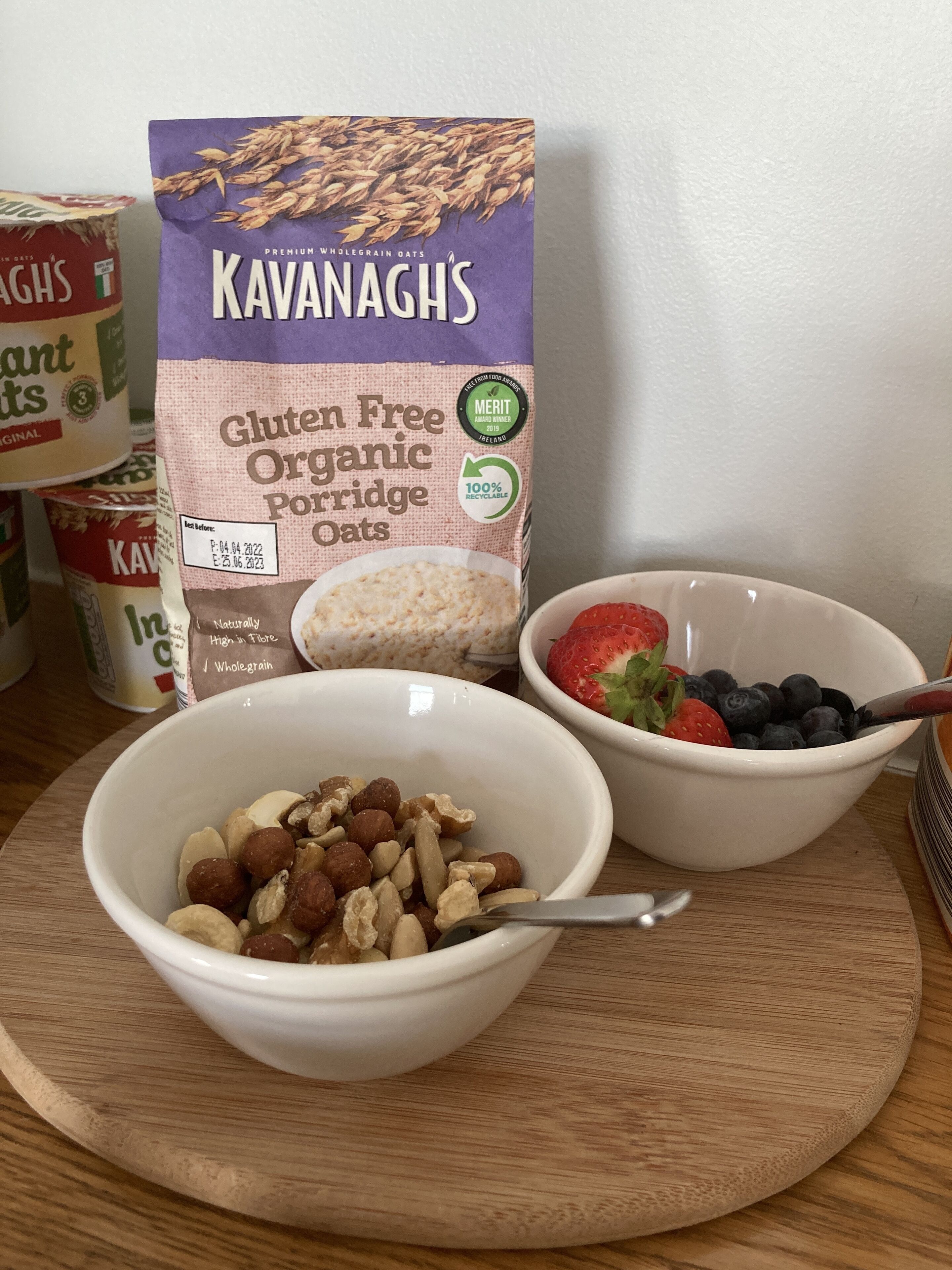 Un cartró de l'avena sense gluten orgànica Kavanagh, un bol de fruits secs i un bol de maduixes i arándanos.