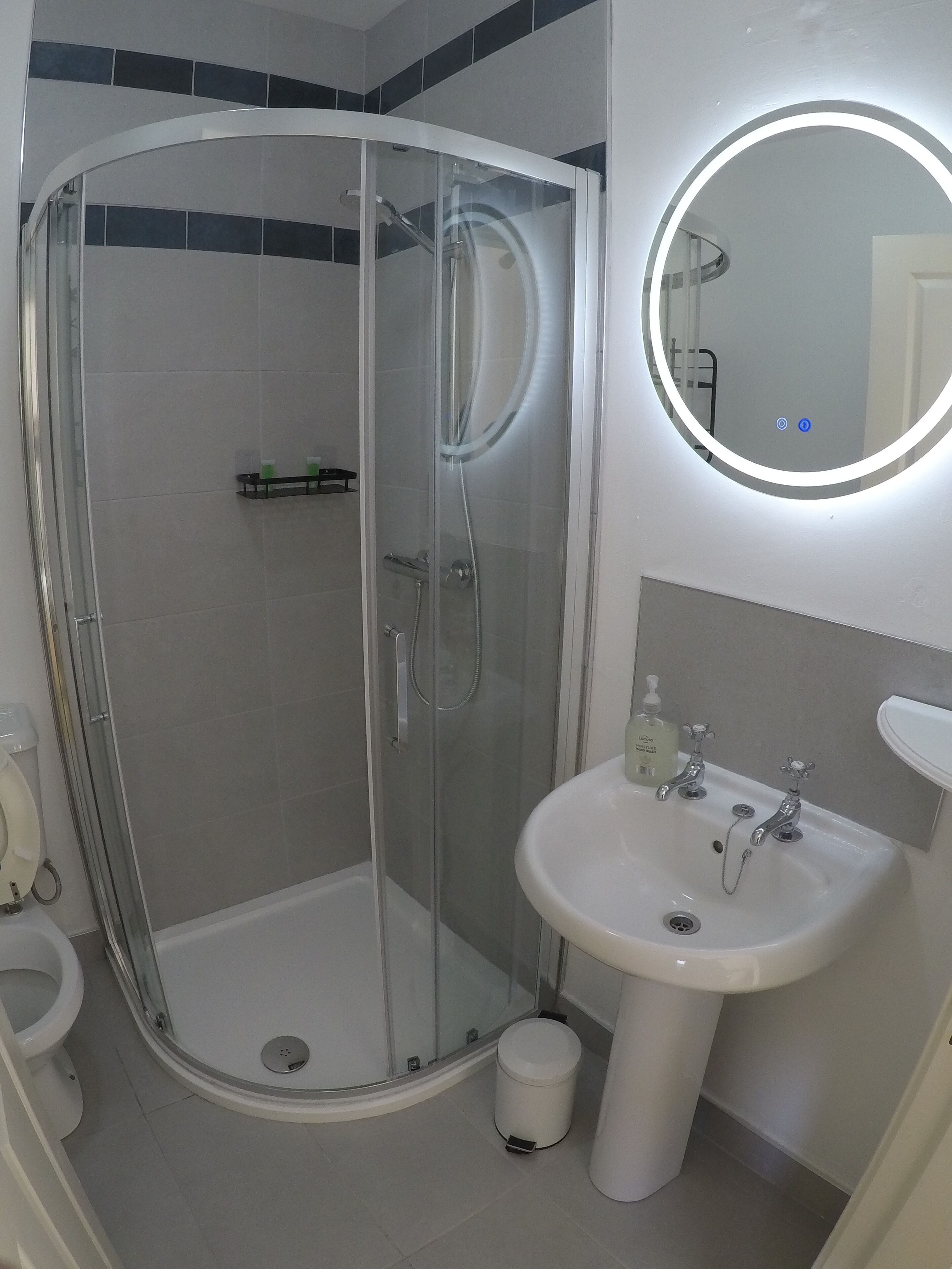 A modern bathroom with a glass-enclosed shower, a white sink with a mirror, and a toilet.