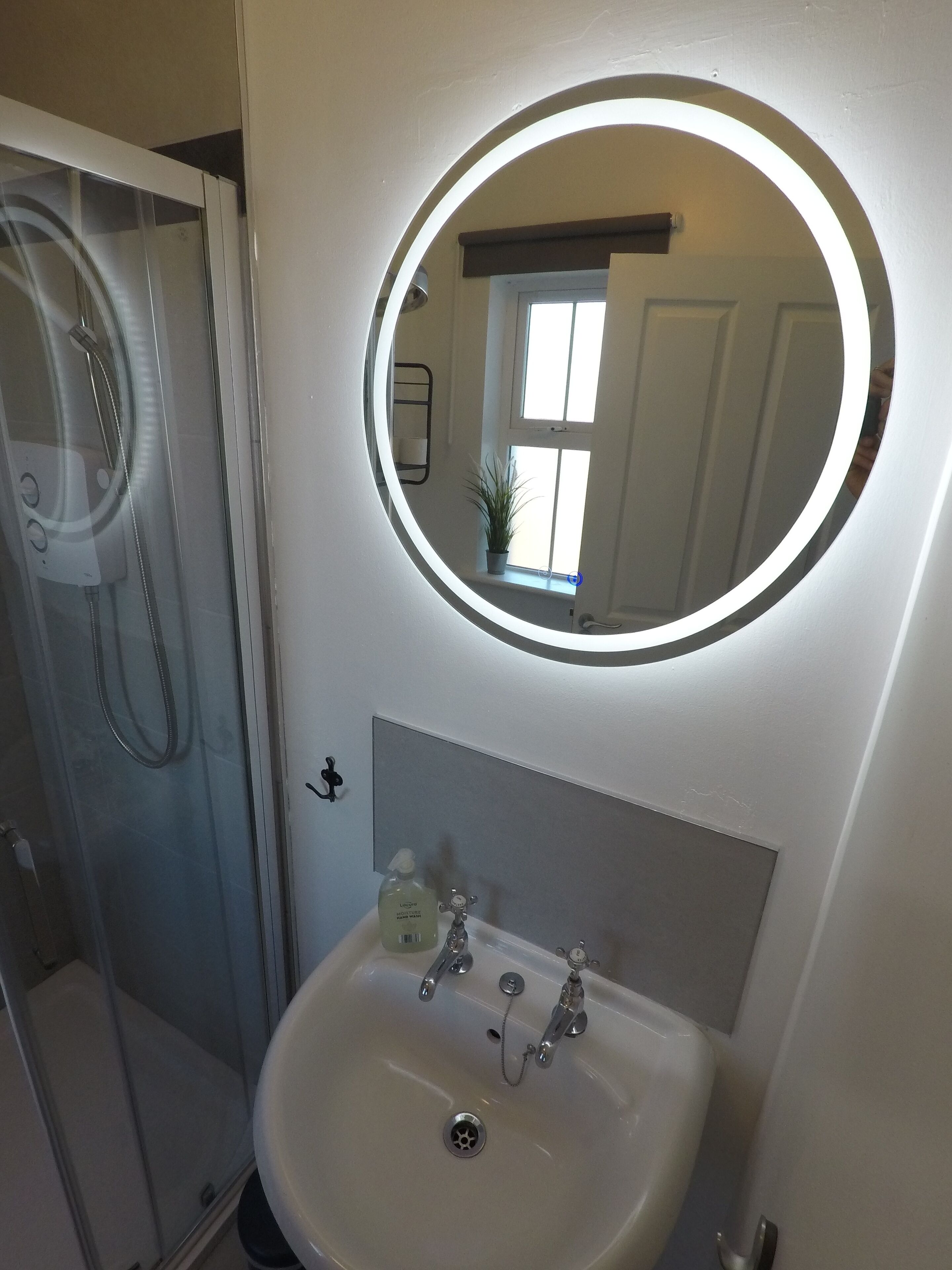A bathroom with a round mirror, a sink, and a shower.