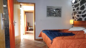 A bedroom with a bed, a nightstand, a lamp, and a stone wall. - Vacation Home Pico Açôres (Calheta de Nesquim)