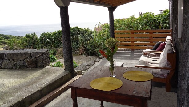 A wooden table with two placemats, a vase with a flower, and a bench with cushions. - Vacation Home Pico Açôres (Calheta de Nesquim)