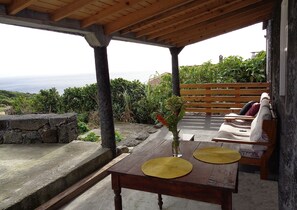 Une table en bois avec deux sets de table, un vase avec une fleur et un banc avec des coussins.