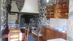 A cozy kitchen with stone walls, wooden cabinets, and a fireplace. There are chairs and a table, suggesting a dining area. - Vacation Home Pico Açôres (Calheta de Nesquim)
