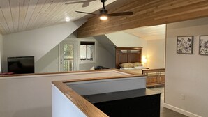 Ein modernes Interieur mit Holzbalkendecke, Deckenventilator, Bett mit Kopfteil, Fernseher und Kunstwerk an der Wand.