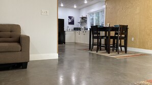 Ein modernes Wohnzimmer mit einer braunen Couch, einem Essbereich mit Tisch und Stühlen sowie einer Küche im Hintergrund.