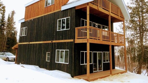 Eine zweistöckige Holzhütte mit einem Balkon im oberen Stockwerk, umgeben von Schnee und Bäumen.