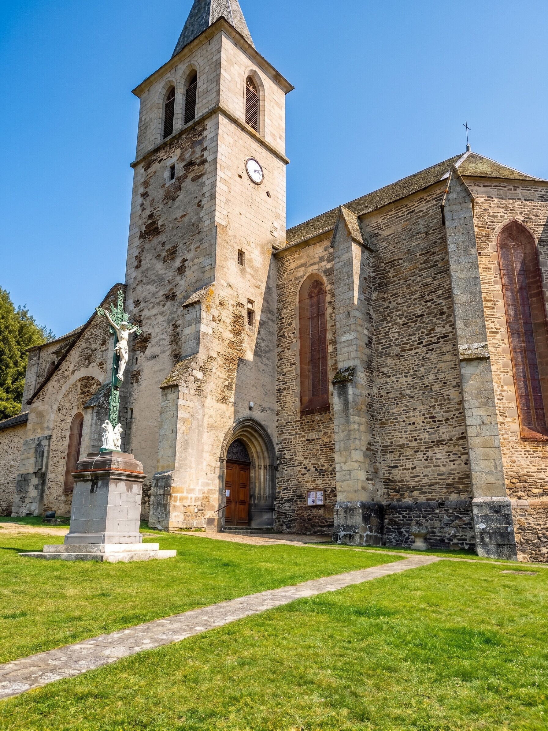 En historisk kyrka med ett högt klocktorn, välvda fönster och en staty i förgrunden.