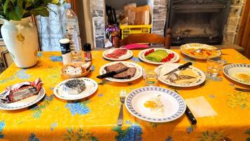 Une table à manger avec différents plats, un vase rempli de fleurs et une cheminée en arrière-plan.