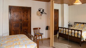 A bedroom with a wooden door, a bed with a patterned bedspread, a chair, a hanging hat, and a mirror. - Homerez - House in Ferrières-Saint-Mary (Ferrières-Saint-Mary)
