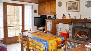 A cozy kitchen with wooden cabinets, a television, a fireplace, and a dining area with a table and chairs. - Homerez - House in Ferrières-Saint-Mary (Ferrières-Saint-Mary)