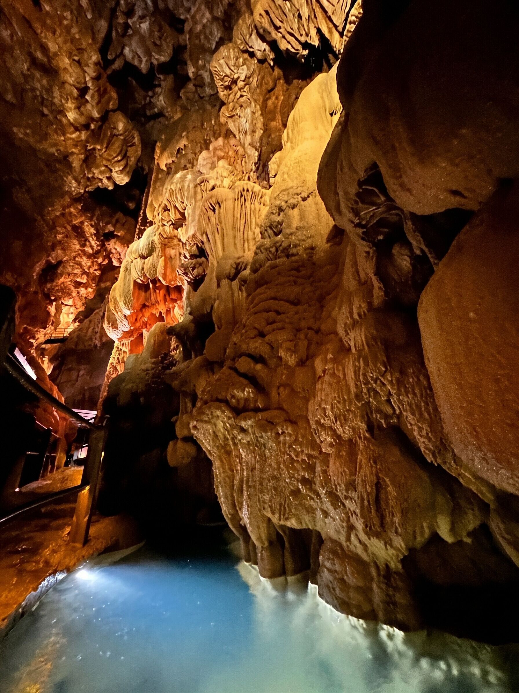 Een grotinterieur met stalactieten, stalagmieten en een waterpoel.