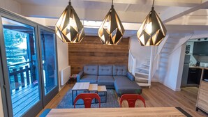 A modern living room with a sectional sofa, a dining table with two chairs, and a kitchen area.