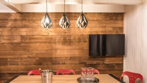 A dining area with a wooden wall, a TV mounted on it, and a table with red chairs.