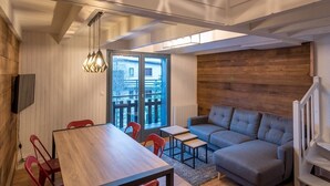 A modern interior with a wooden dining table, red chairs, a grey sofa, and a unique geometric ceiling light fixture.