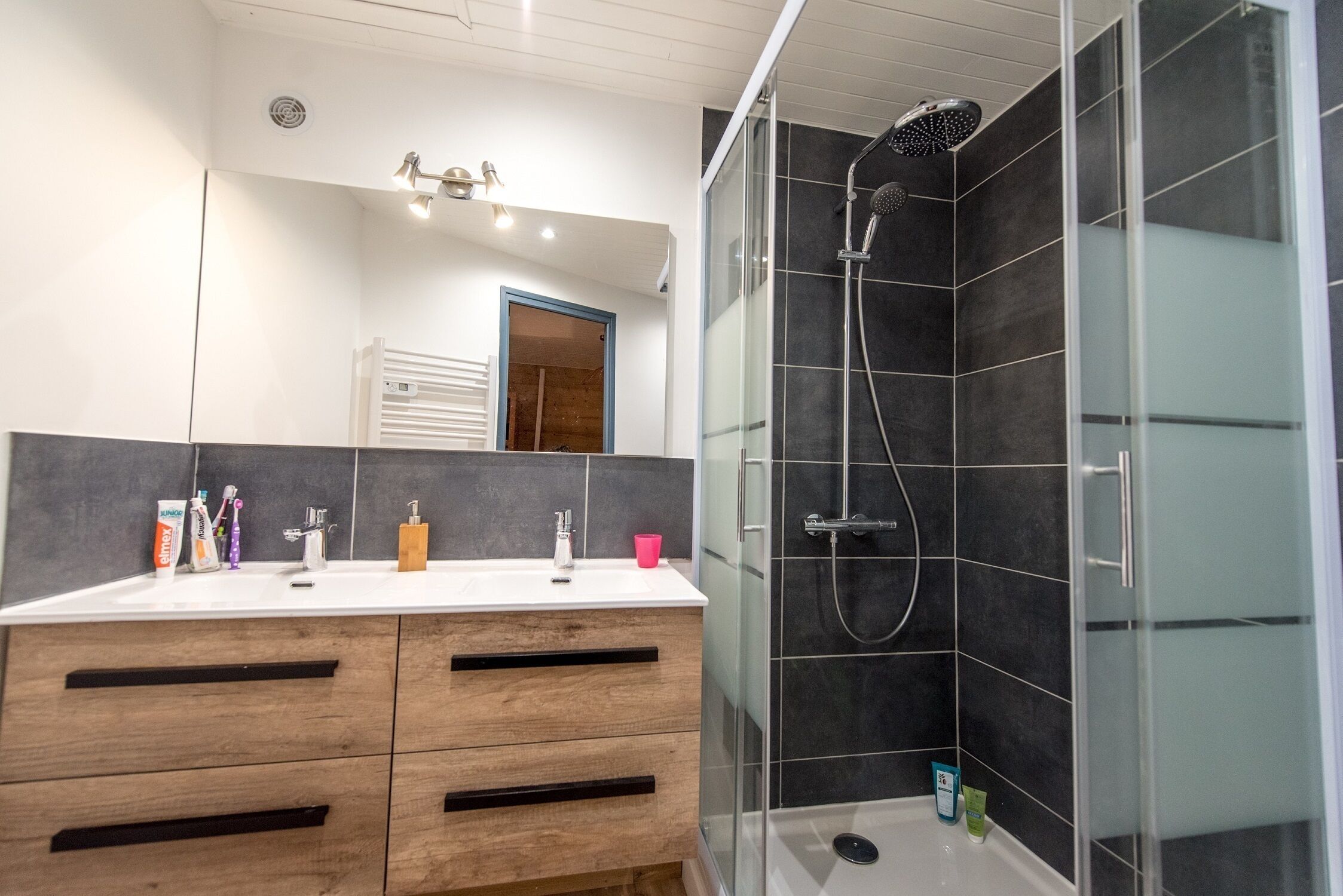 Une salle de bain moderne avec un meuble-lavabo blanc, une douche carrelée aux tons foncés et un espace de douche délimité par des parois en verre.
