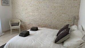 A bedroom with a brick wall, a white bed with pillows, a chair, and a lamp. - Architect house with swimming pool, village heart, 3 km from the beaches (Saint-Georges-d'Oléron)