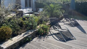 A patio with a stone wall, lounge chairs, and a white building with a stone facade. - Architect house with swimming pool, village heart, 3 km from the beaches (Saint-Georges-d'Oléron)