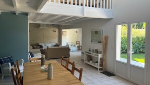 A spacious living area with a high ceiling, a dining table with chairs, a sofa, and a staircase leading to an upper level. - Architect house with swimming pool, village heart, 3 km from the beaches (Saint-Georges-d'Oléron)