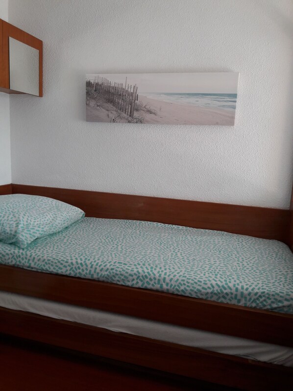 A single bed with a patterned bedspread, a wooden headboard, and a framed picture of a beach scene on the wall. - Studio 4 pers sea view, parking, wifi, air conditioning, household linen provided. (Hyères)