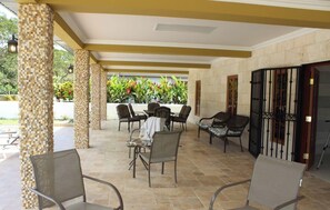 Un espace extérieur aménagé avec des chaises et des tables, un sol carrelé et une vue sur la verdure.
