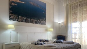 A bedroom with a large bed, two bedside tables, a nightstand, a window with curtains, and a cityscape painting on the wall. - Alice's House Luxury Hospitality - Elevator & Fast Wi-fi (Siracusa)