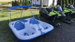 A small inflatable boat with a canopy, a kayak, and two snowmobiles parked on a gravel path. - Majestic Recreational Lodging w/ Snowmobile and Side x Side rentals on Long Lake (Sinclair)